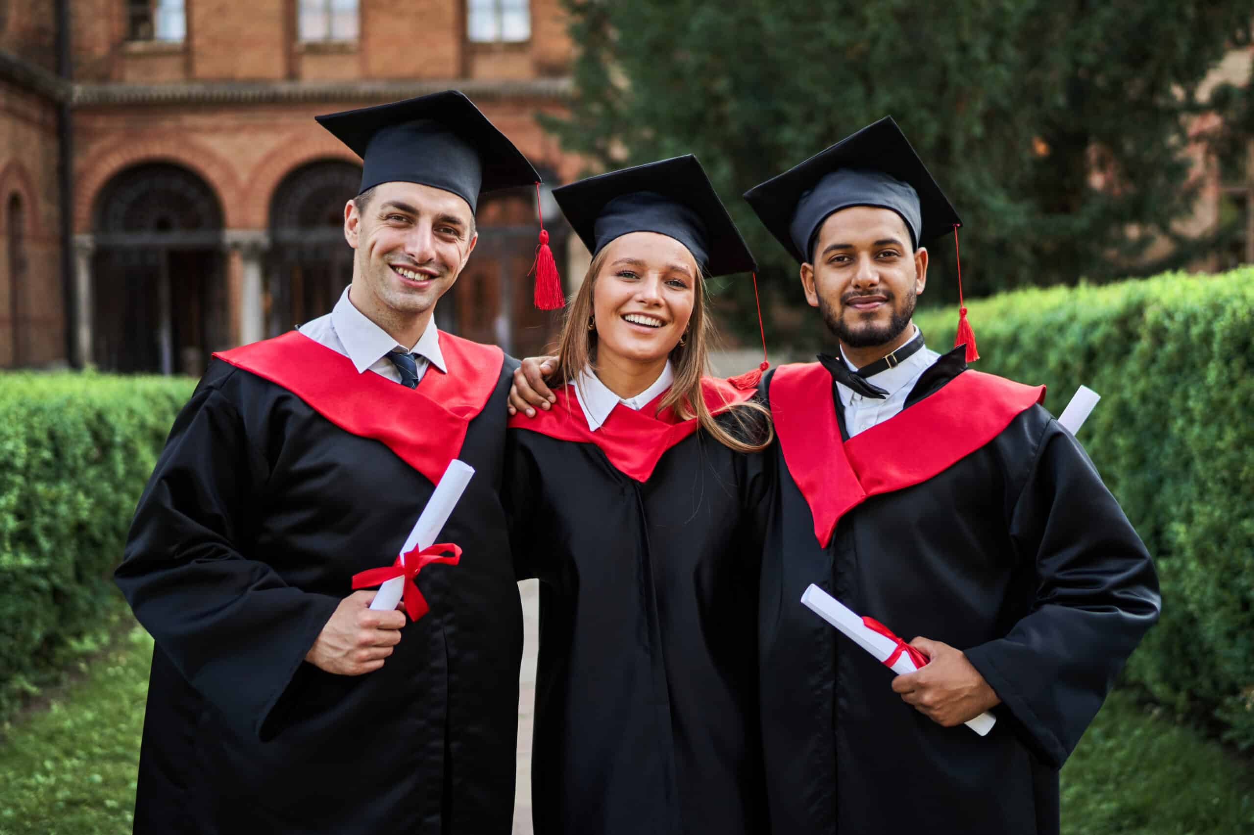 Portrait of three smiling graduate friends in graduation robes i
